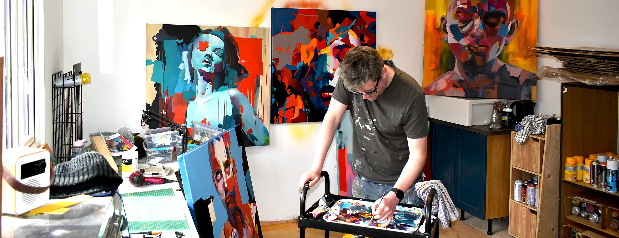 Paul Kneen painting in his studio surrounded by abstract portrait paintings